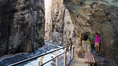 People on a bridge in a gorge, surrounded by rocks and a flowing stream.