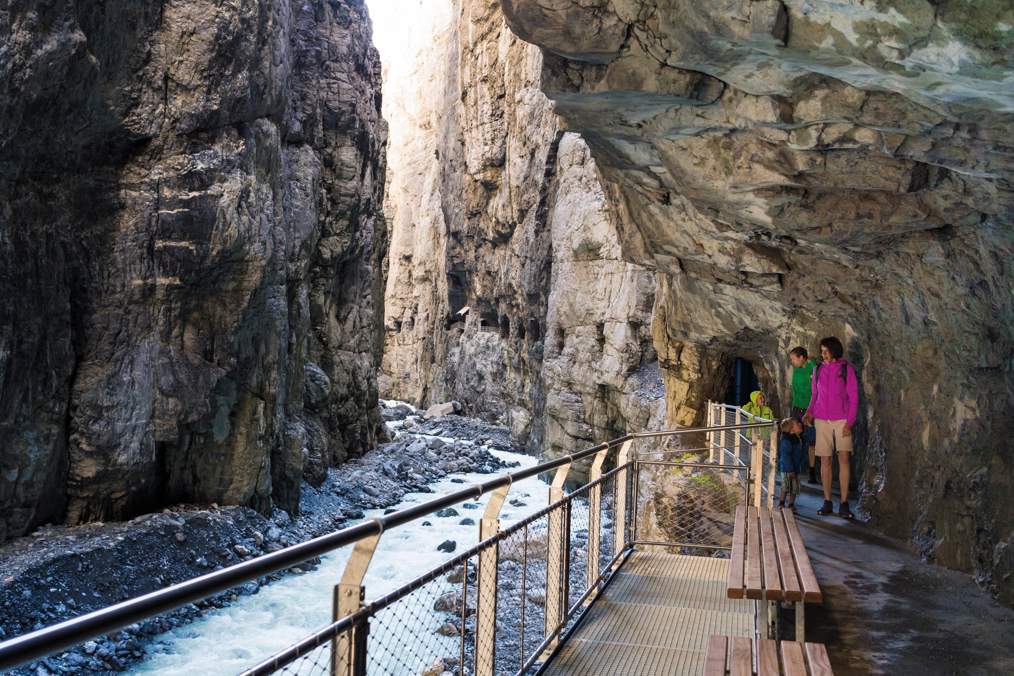 People on a bridge in a gorge, surrounded by rocks and a flowing stream.