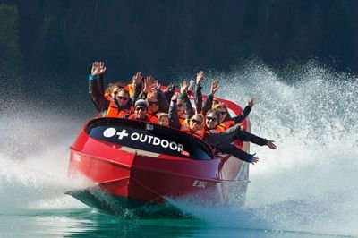 Personen in einem roten Jetboot mit Schwimmwesten auf einem See, umgeben von spritzendem Wasser.