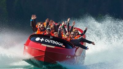 Personen in einem roten Jetboot mit Schwimmwesten auf einem See, umgeben von spritzendem Wasser.
