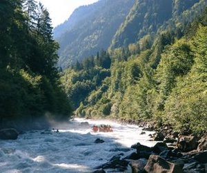 Rafting group in helmets and life jackets navigates rapids in a forested river area in the Jungfrau region.