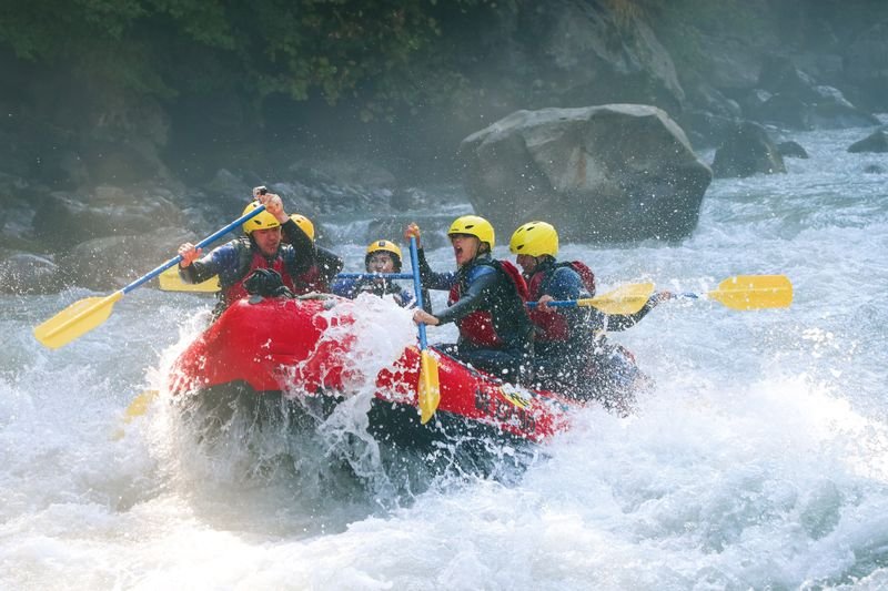 River rafting in whitewater on the Lütschine. Participants wear life jackets and sit paddling in a red raft