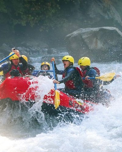 River rafting in whitewater on the Lütschine. Participants wear life jackets and sit paddling in a red raft