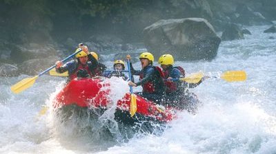 River-Rafting im Wildwasser auf der Lütschine. Teilnehmer tragen Schwimmweste und sitzen paddelnd in einem roten Schlauchboot