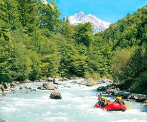 River rafting on the Lütschine with helmets and paddles, surrounded by lush forest and snow-covered mountains in the background