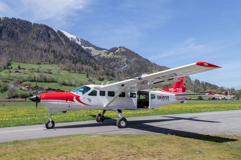 Ein rotes und weißes Flugzeug steht auf einer Landebahn vor einer Berglandschaft.