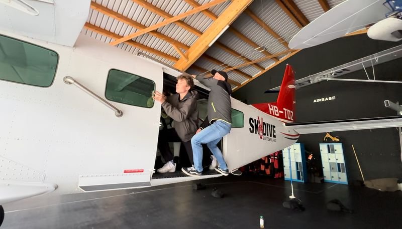 Two people board an airplane in a hangar, visible are airplane doors and wings.